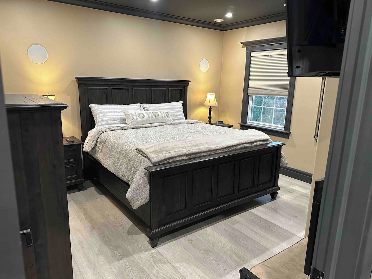 Een slaapkamer met een donker houten bed, nachtkastjes, een raam met zonwering en een aan de muur bevestigde televisie.