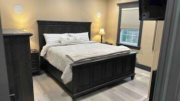 Een slaapkamer met een donker houten bed, nachtkastjes, een raam met zonwering en een aan de muur bevestigde televisie.