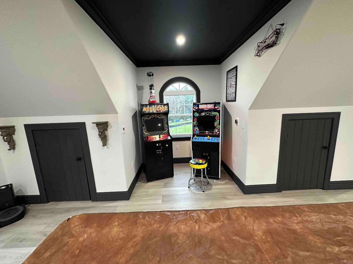 Quarto com duas máquinas de jogos eletrônicos, um banquinho pequeno e uma janela com vista.