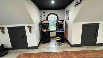 Quarto com duas máquinas de jogos eletrônicos, um banquinho pequeno e uma janela com vista.