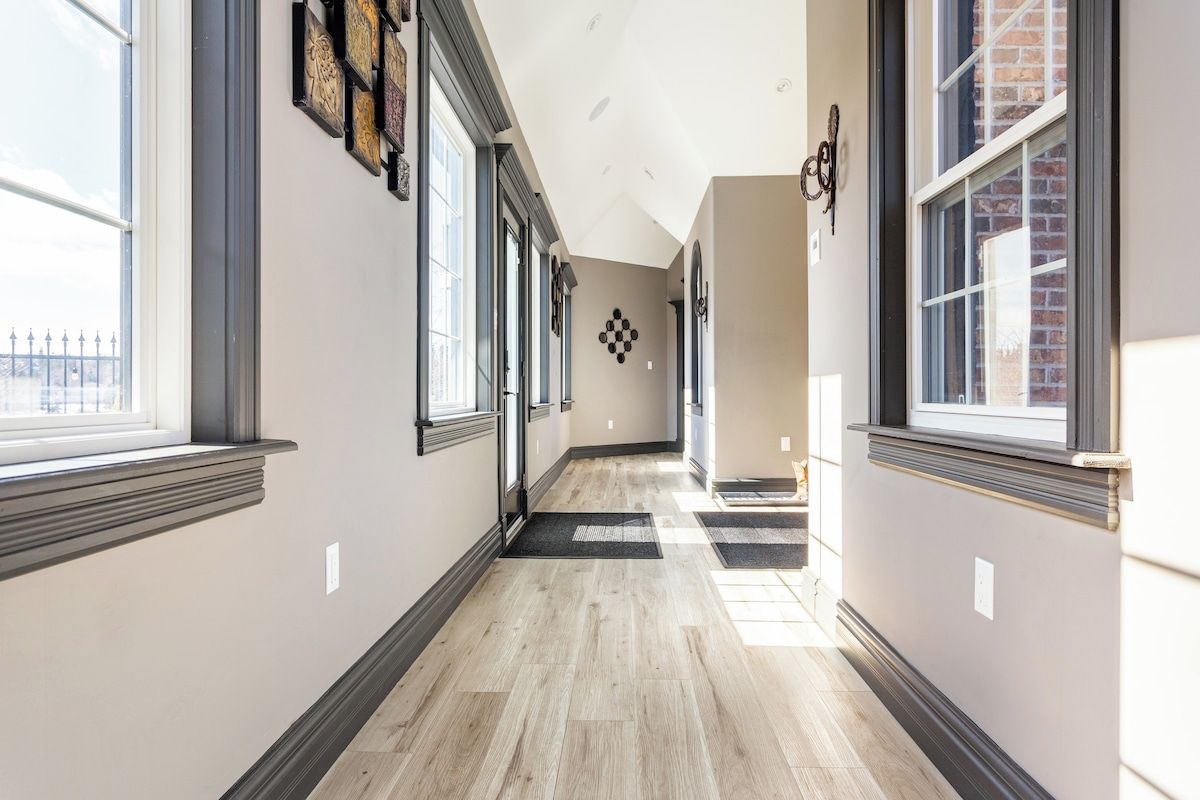 A hallway with large windows, a checkered wall decoration, and a wooden floor.