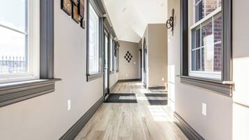 A hallway with large windows, a checkered wall decoration, and a wooden floor.