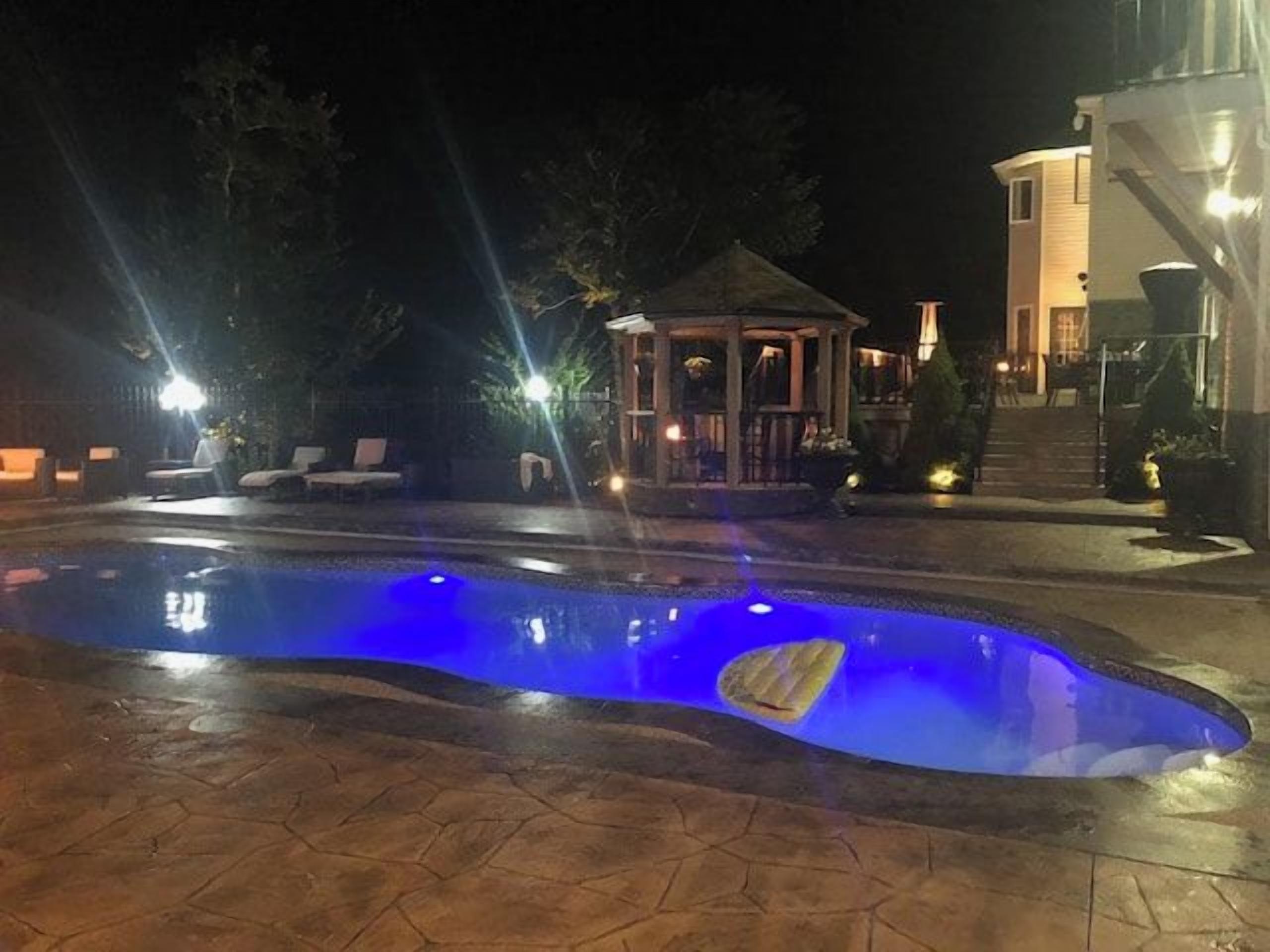 Una piscina con iluminación azul, rodeada de sillas de descanso y un pabellón.