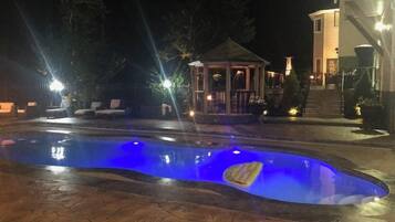 Piscina com iluminação azul, cercada por espreguiçadeiras e um gazebo.