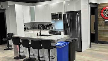 Een moderne keuken met een centraal eiland, barkrukken, roestvrijstalen apparatuur en een prullenbak.