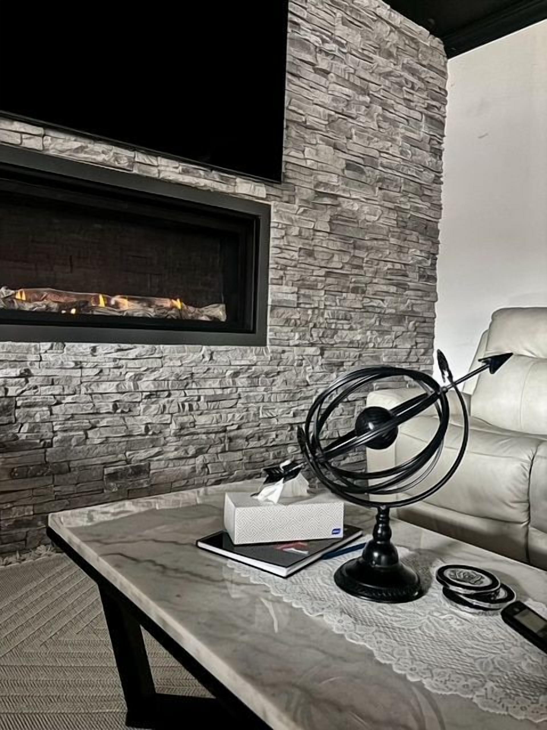 A room with a stone wall, a fireplace, a leather couch, and a table with a lamp and a tissue box.