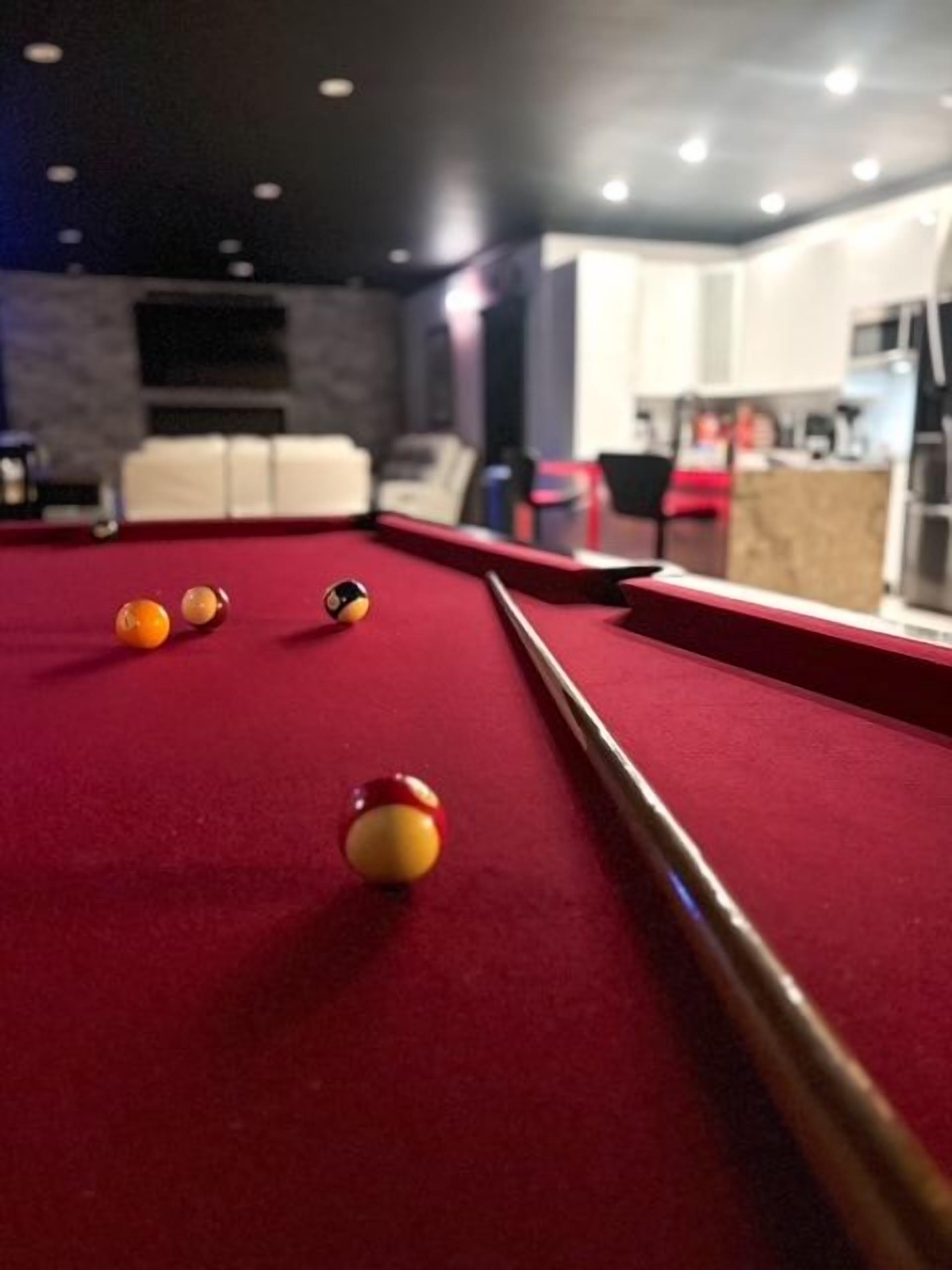 A pool table with balls, a pool cue, and a red felt surface.