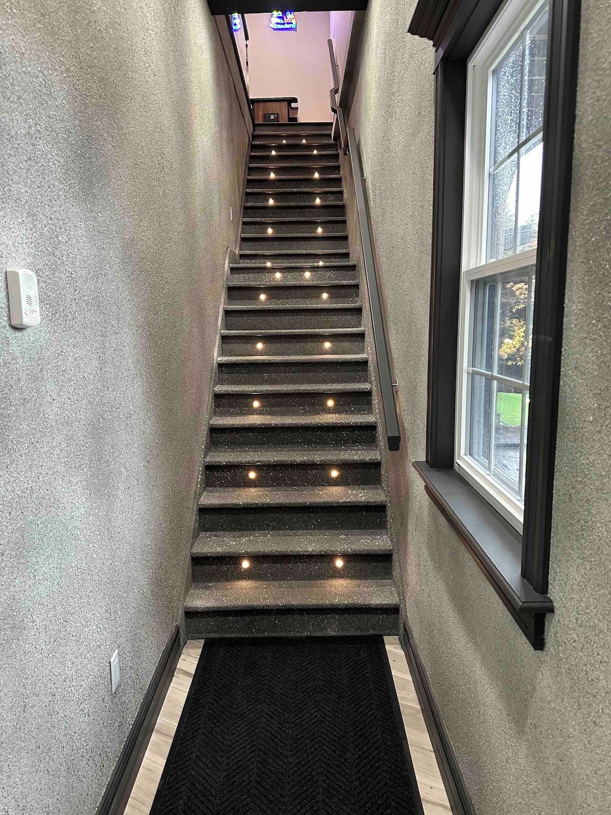 A staircase with handrails and lights, leading to a landing with a bench and a sign.