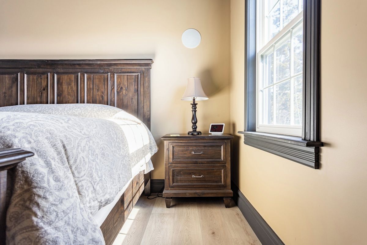 A bedroom with a bed, a nightstand with a lamp, and a window with blinds.