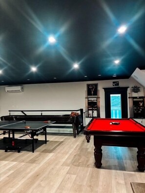 A billiards room with a pool table, a snooker table, and a dartboard.