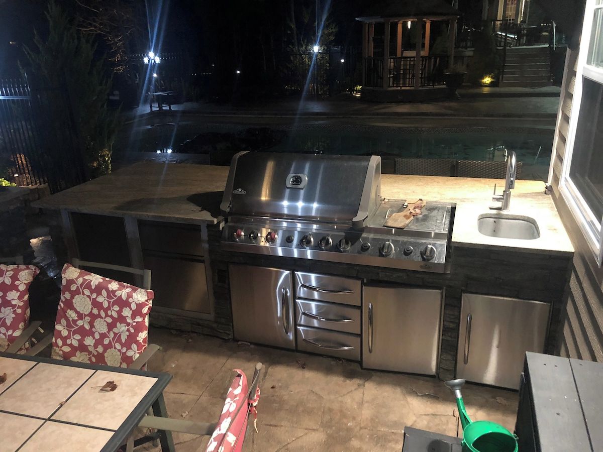An outdoor kitchen with a grill, sink, and storage cabinets.