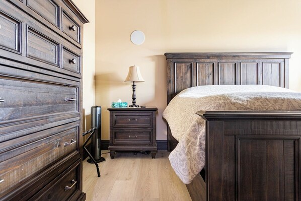 A bedroom with a dark wooden bed, a dresser, a nightstand with a lamp, and a small table with decorative items. - Luxury Lakefront Suite - Hot Tub & Amenities! (Hammonds Plains)