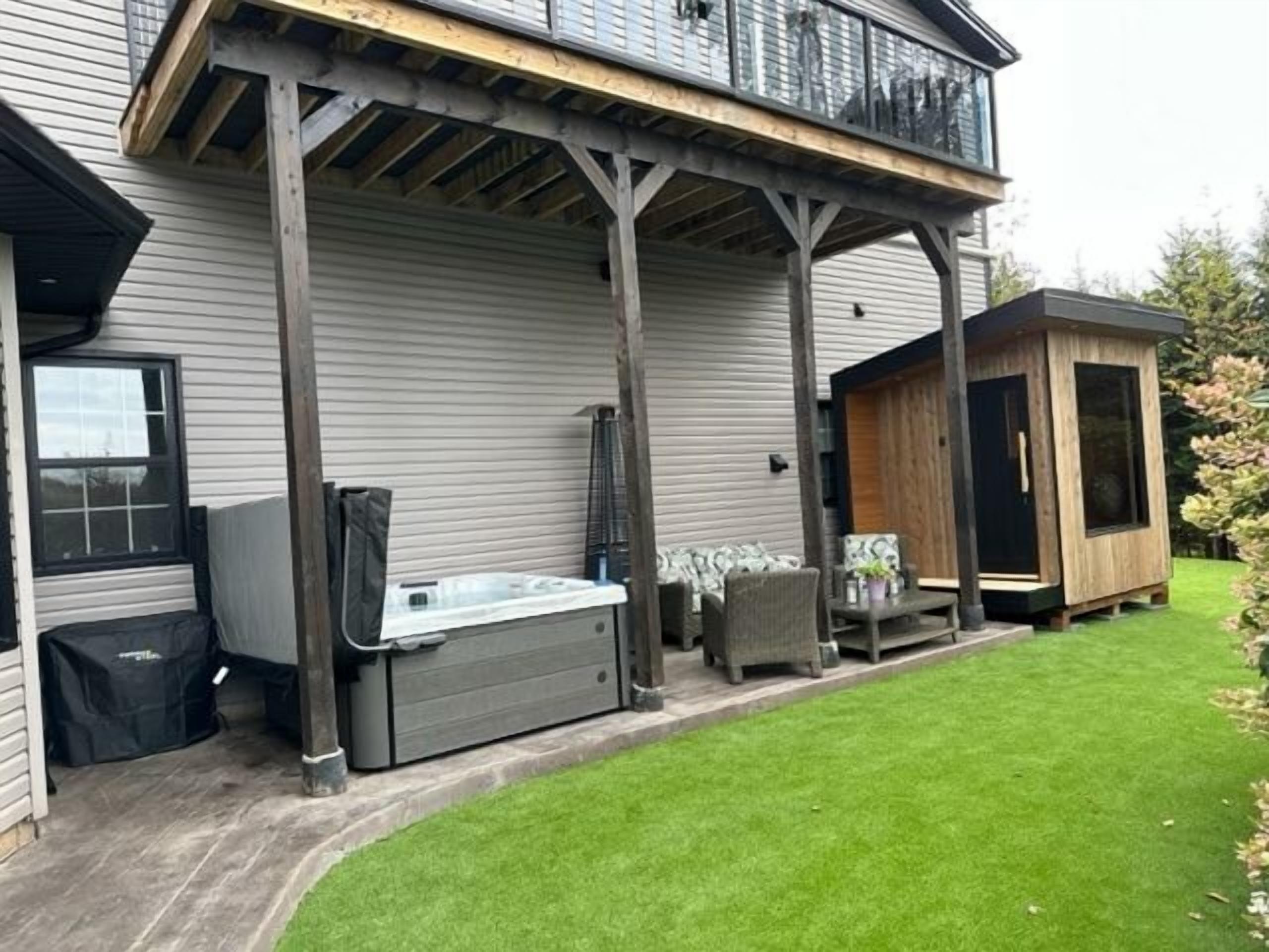 Una casa con porche cubierto, jacuzzi y una pequeña construcción de madera.