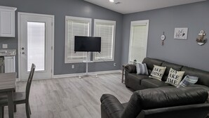 A living room with a dark leather couch, a flat-screen TV mounted on a stand, and a dining area with a wooden table and chairs. - Brand New Floating Home on Norris Lake : Sleeps 12 : Swim, Grill & Relax! #3 (LaFollette)