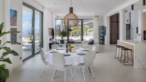 Een moderne eetruimte met een grote tafel voor zes personen, een bar met krukken en een uitzicht op de natuur door grote ramen.