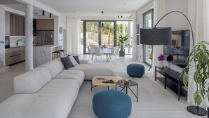 Een moderne woonkamer met een modulaire bank, een salontafel en een tv-meubel. Achtergrond toont een eethoek met een tafel en stoelen.