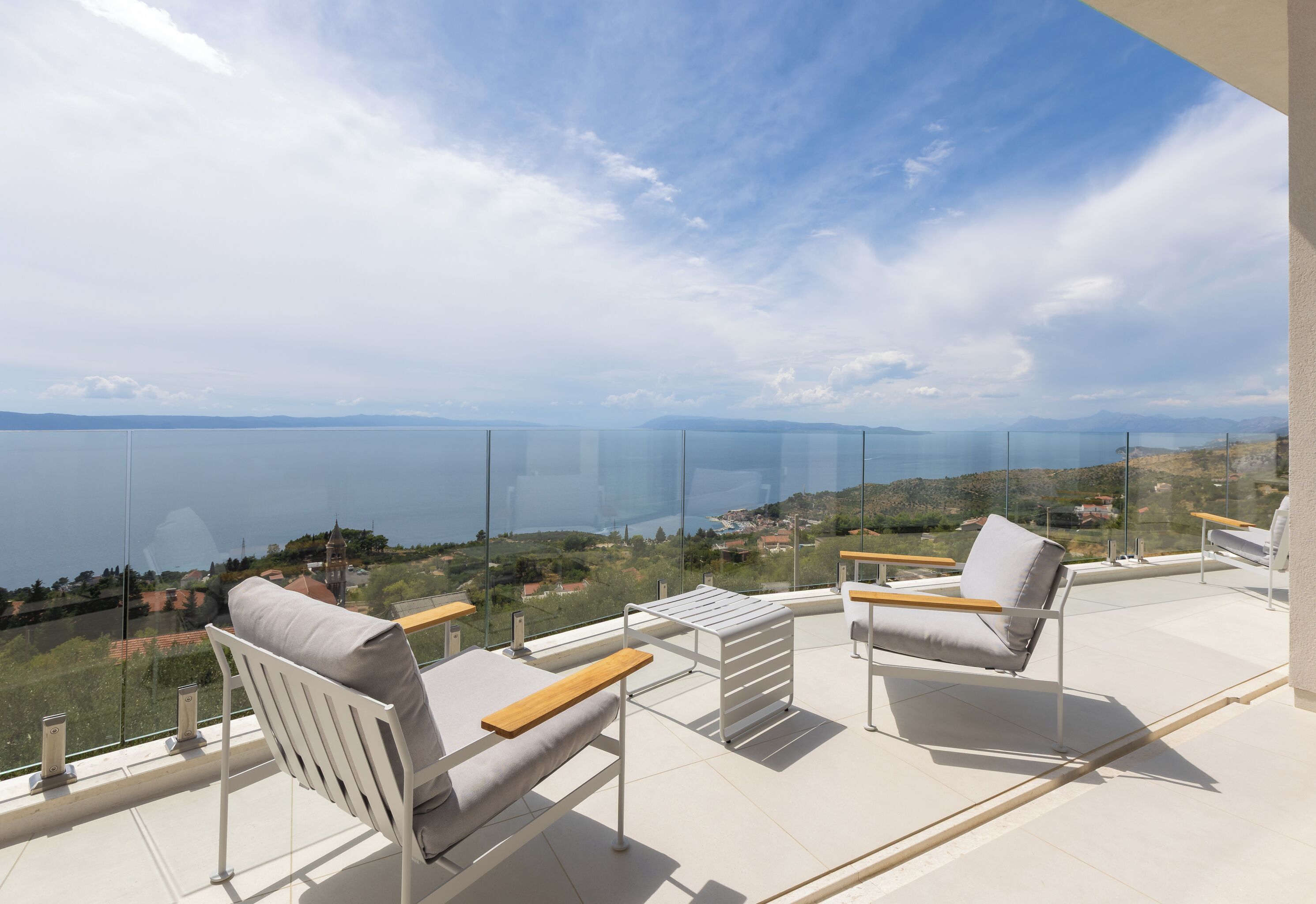 Un balcon avec deux chaises et une table, offrant une vue panoramique sur une étendue d’eau et un paysage lointain.