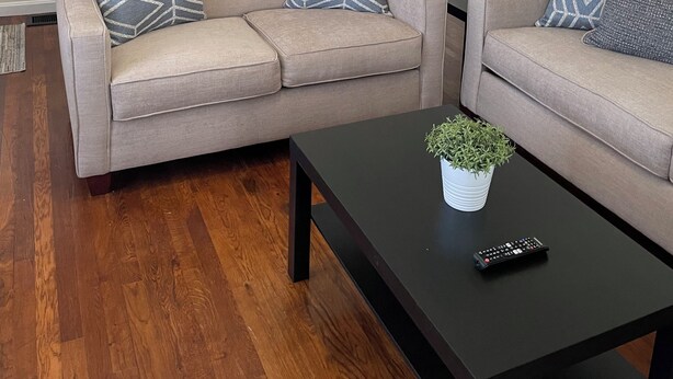 A living room with two beige sofas, a black coffee table, and a staircase with a mirror.