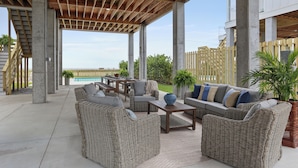 An outdoor patio area with wicker furniture, concrete pillars, and a view of a pool.