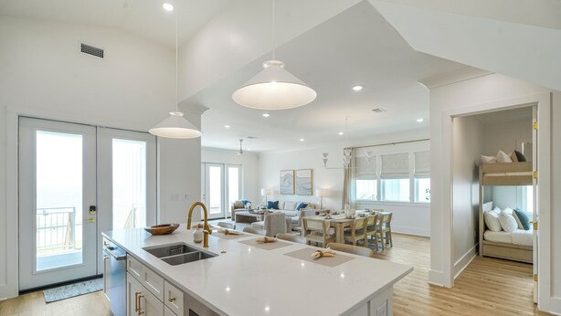 A spacious kitchen with a large island, modern pendant lighting, and a view to the living area.