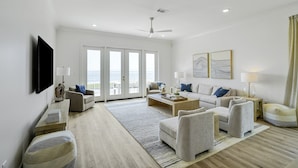 A spacious living room with a large window, a ceiling fan, and a flat-screen TV mounted on the wall.