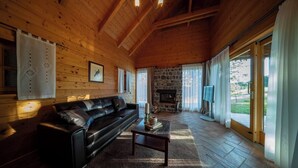 A cozy cabin interior with a stone fireplace, wooden walls, a leather sofa, and a large window. - Posestvo Pule Equestrian Estate (Mokronog-Trebelno)