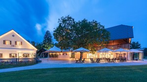 A hotel with a large tree in the center, outdoor seating area, and a well-lit patio. - Posestvo Pule Equestrian Estate (Mokronog-Trebelno)
