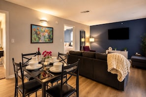 A modern living room with a dining area, a dark blue accent wall, a flat-screen TV, and a cozy fireplace. - Spacious Austin 3BR Home · Workspace · Sleeps 12 · 10min to UT (Austin)