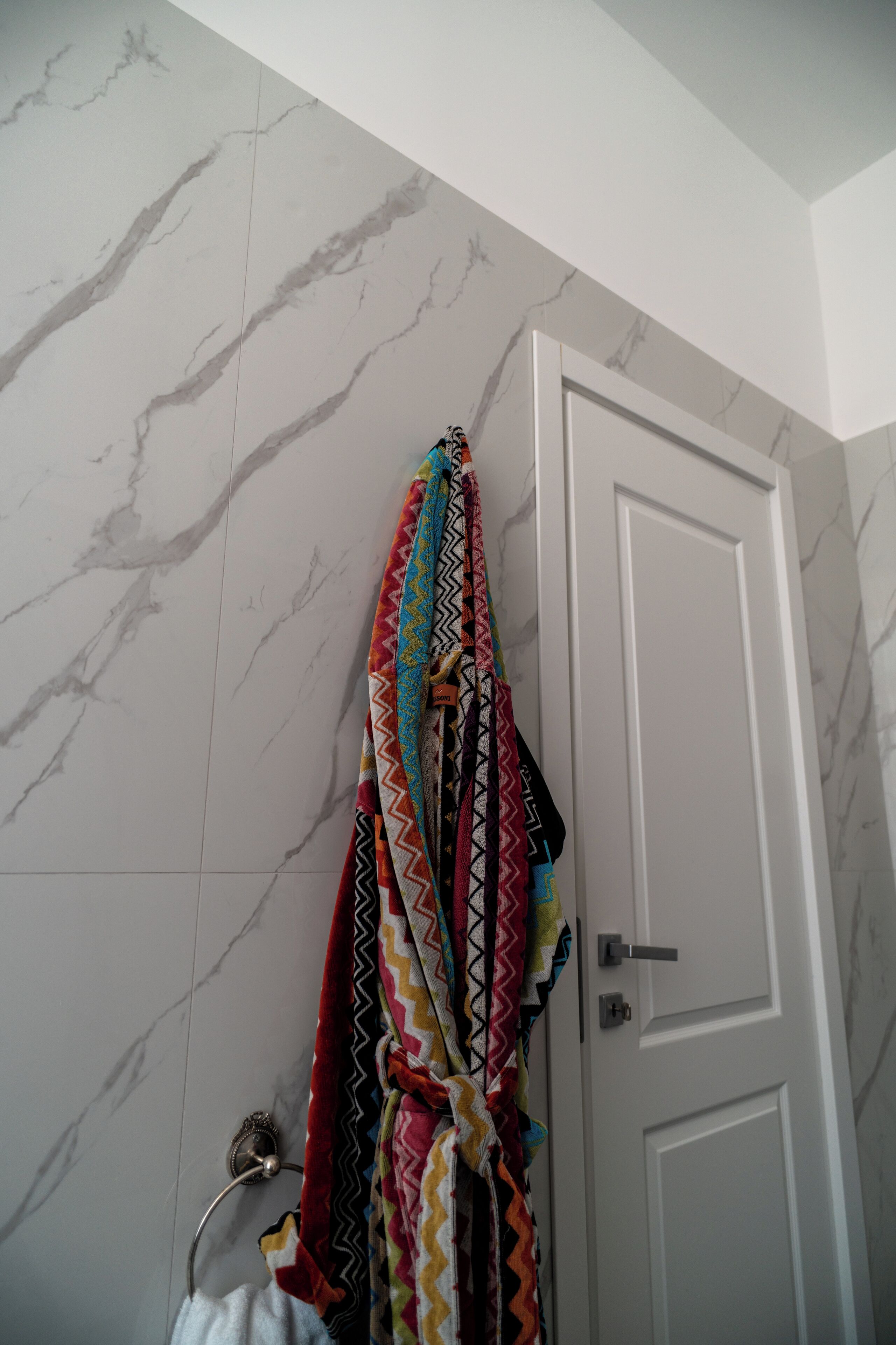 Un bagno con parete in marmo, una porta bianca e un asciugamano colorato appeso a un porta asciugamani.