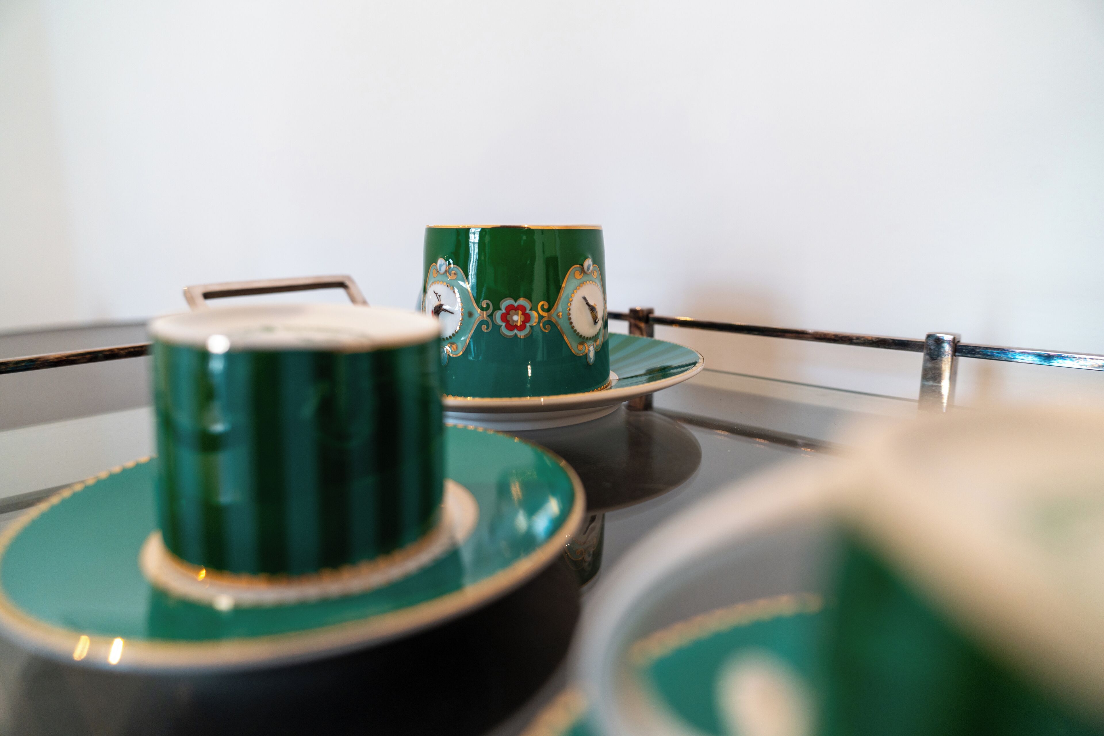 A close-up of a green teapot and cup set on a reflective surface.