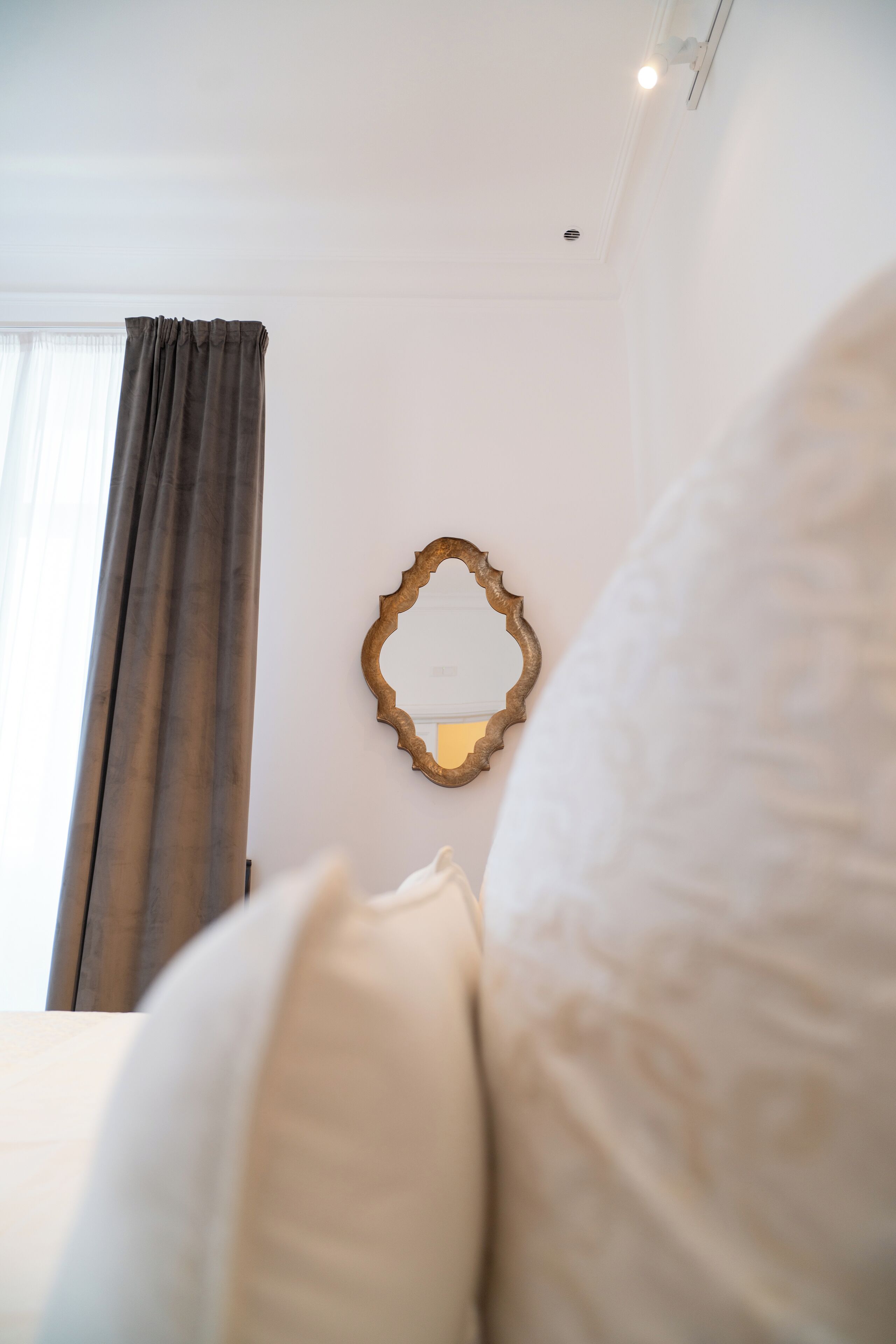 A bedroom with a large bed, a mirror, and a window with curtains.