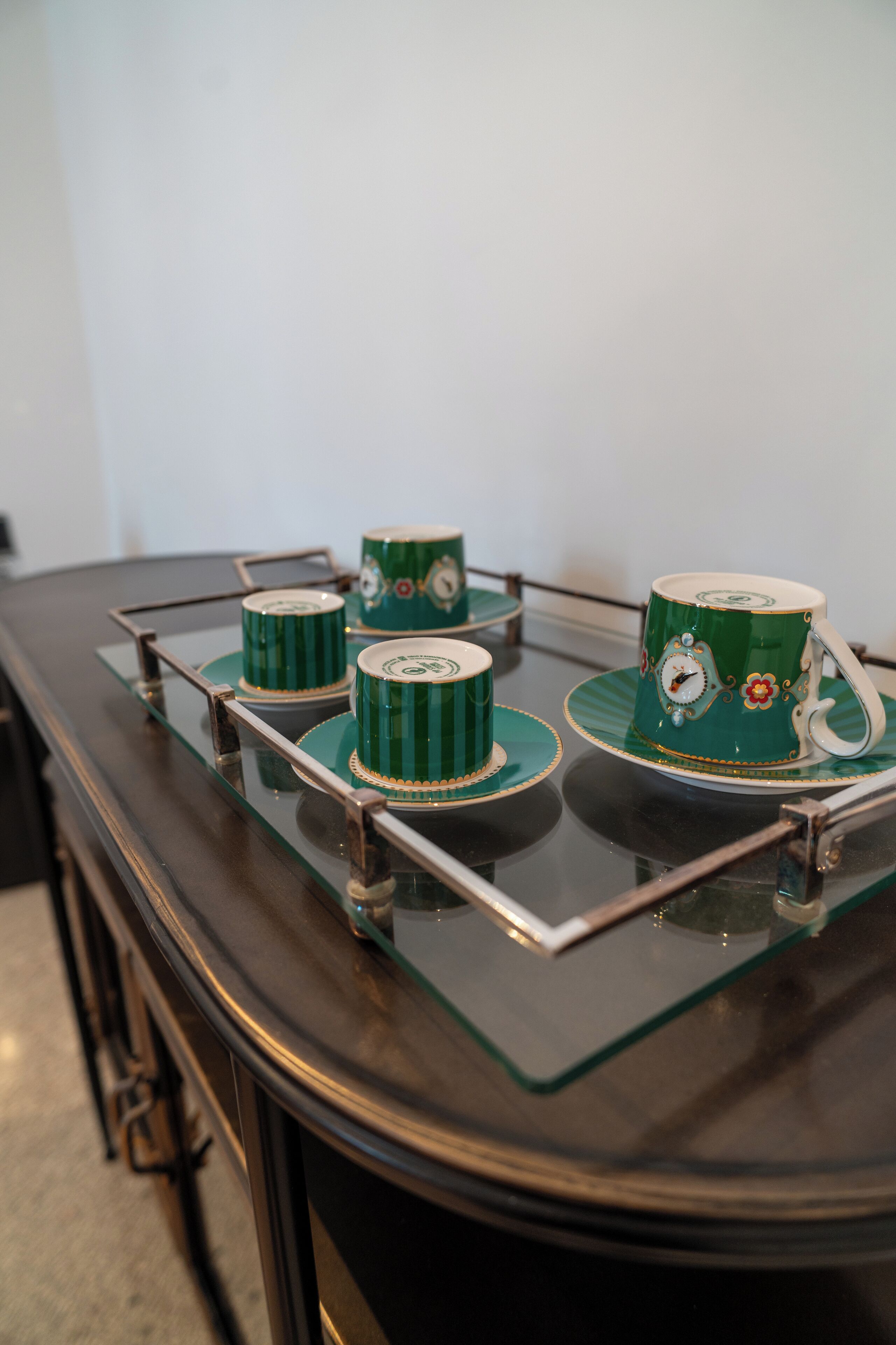 A glass-top table with four green cups and saucers, each with a floral design.