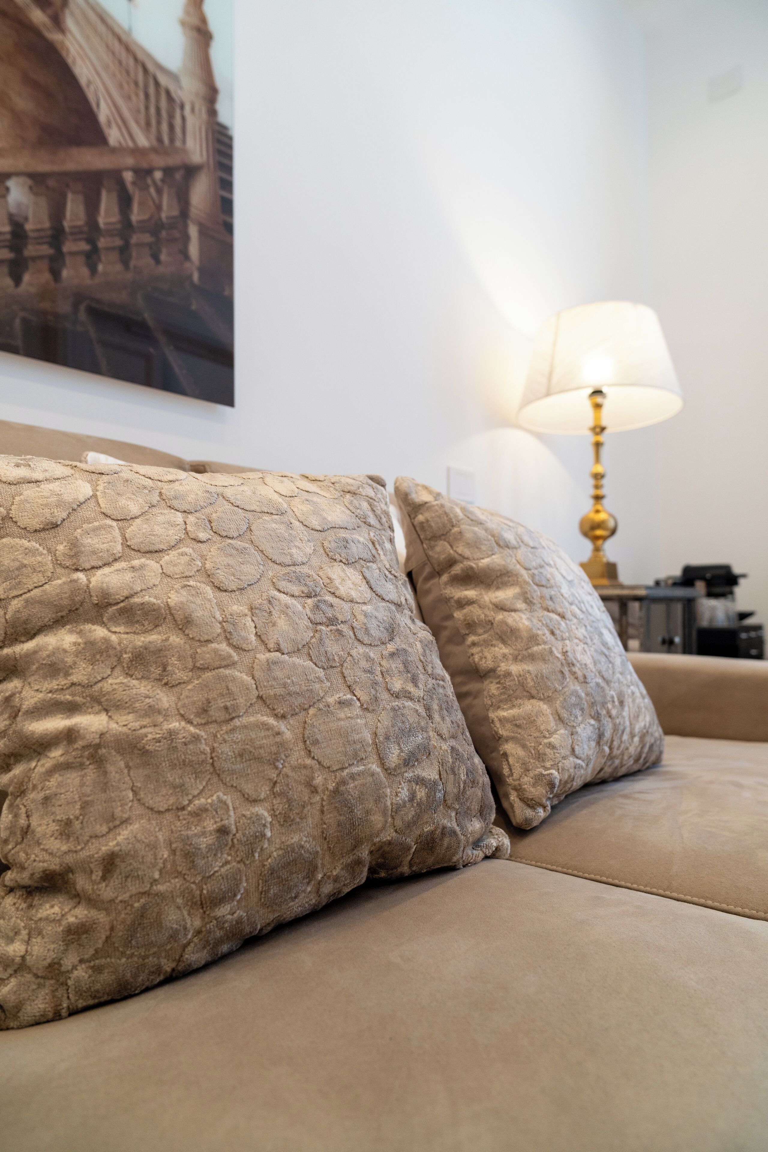 En beige sofa med strukturerede puder og en guldfarvet lampe i baggrunden.