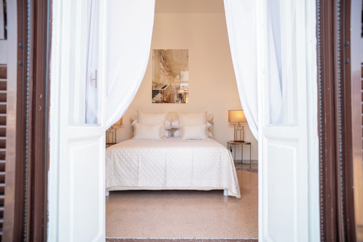 A bedroom with a large bed, white bedding, and a painting on the wall.