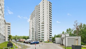Ein Hochhaus mit mehreren Balkonen, einem Parkplatz und einem kleinen Garten.