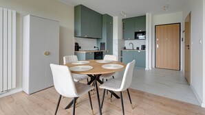 Eine moderne Küche mit Essbereich, ausgestattet mit einem runden Tisch mit weißen Stühlen, einem eingebauten Backofen und grünen Schränken.