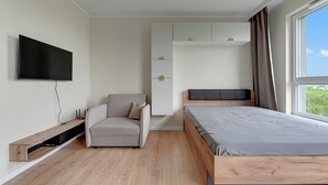 Ein modernes Schlafzimmer mit Bett, Wand-Fernseher, eingebautem Sitzplatz und einem Fenster mit Vorhängen.