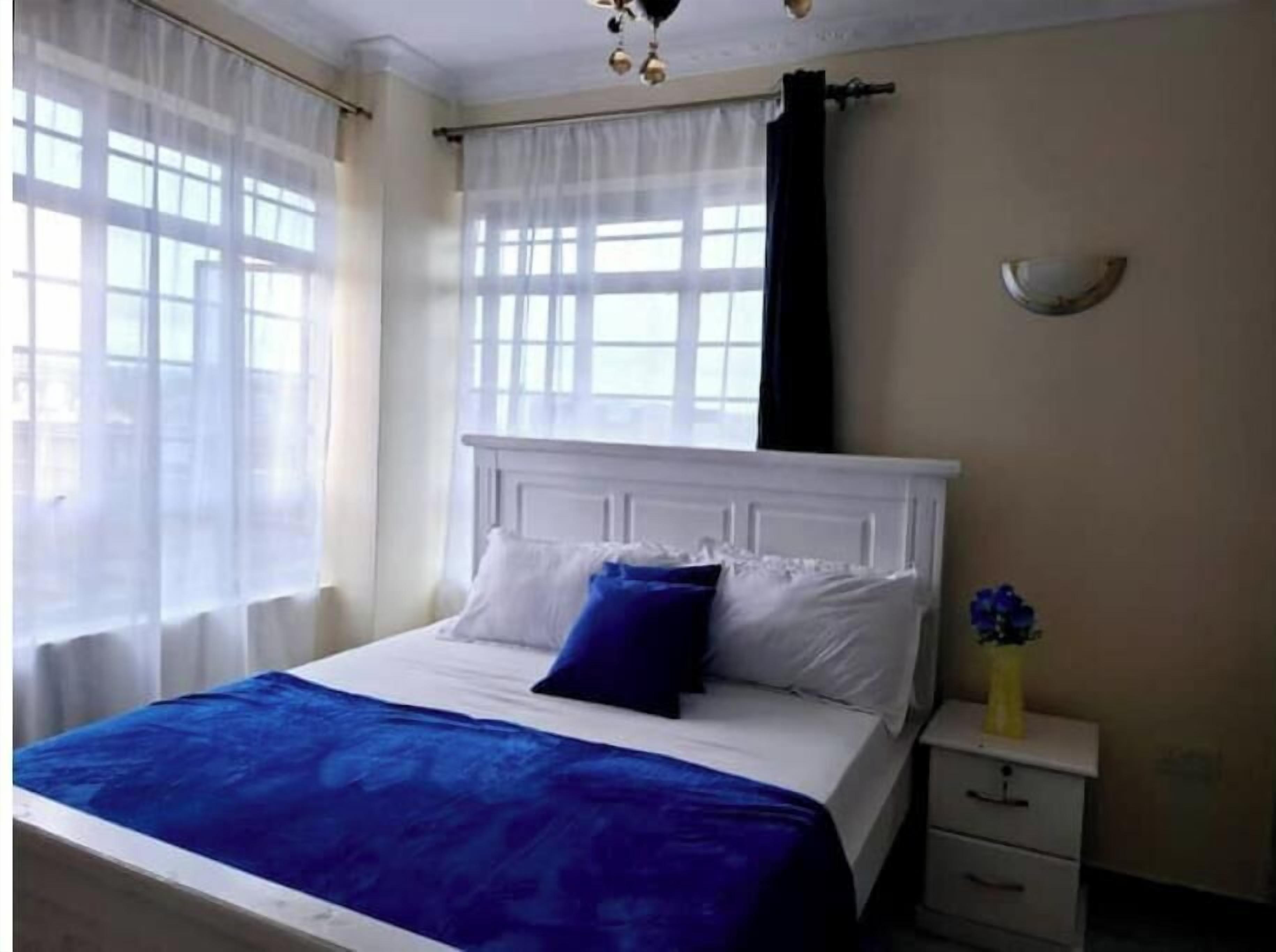 Un dormitorio con cama, cortinas blancas, una mesita de noche y un jarrón con flores.
