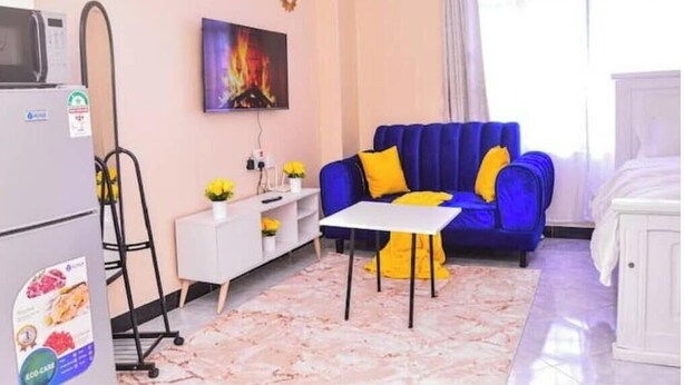 Un espace de vie compact comprenant un canapé bleu, une petite table blanche, un meuble blanc, un four à micro-ondes et un téléviseur fixé au mur.