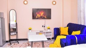 Une chambre avec un lit, un téléviseur fixé au mur, un bureau blanc et un canapé bleu avec des coussins jaunes.