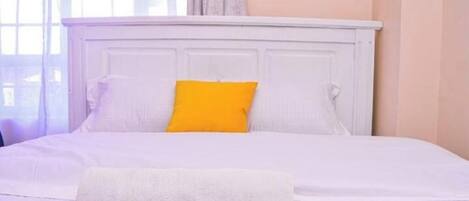 A neatly made bed with white bedding and a single bright yellow pillow.