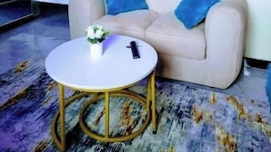 A hotel room with a sofa, a small round table with a vase, a bed, a mirror, and a door. - Elegant Studio (Kiambu)