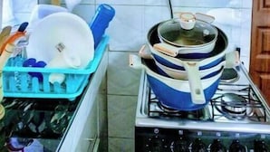 A kitchen with a gas stove, a pot on the stove, a dish rack with dishes, and wooden cabinets. - Elegant Studio (Kiambu)