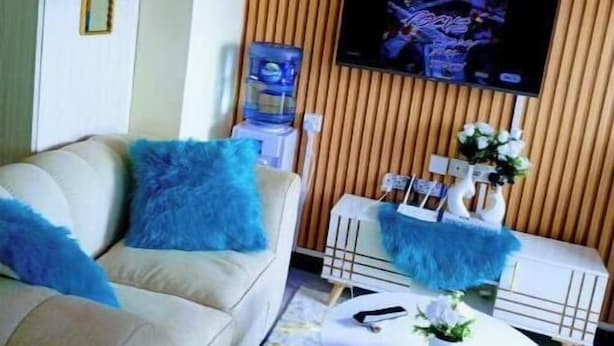 A living room with a sofa, coffee table, and a flat-screen TV mounted on a wooden wall. - Elegant Studio (Kiambu)