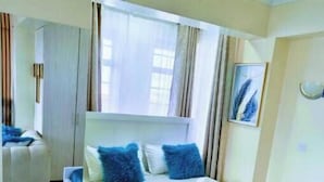 A bedroom with a bed, a chair, a mirror, and a window with curtains. - Elegant Studio (Kiambu)