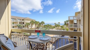 A balcony with a table set for two, overlooking a beach with palm trees and a view of the ocean. - MyStay at 222 Breakers | Romantic Oceanfront Villa + Heated Pool (Hilton Head Island)
