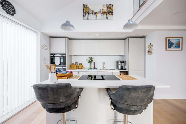Une cuisine moderne avec des meubles blancs, un îlot central et deux tabourets de bar.