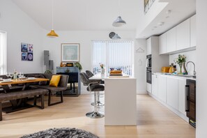 Eine moderne Küche mit weißen Schränken, einer zentralen Kochinsel und einem Essbereich mit Holztisch und dunklen Stühlen.