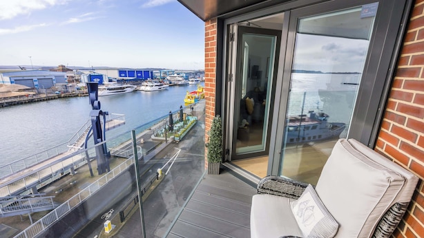 Un balcon avec un canapé blanc et une porte vitrée, donnant sur une marina avec des bateaux et un pont.