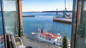 Une vue depuis un balcon donnant sur une marina, avec un bateau amarré, une grue et un ciel dégagé.